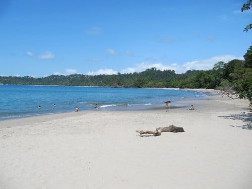 Visitors relax on the wide sandy shore and calm waters of Playa Espadilla Sur in Manuel Antonio National Park.