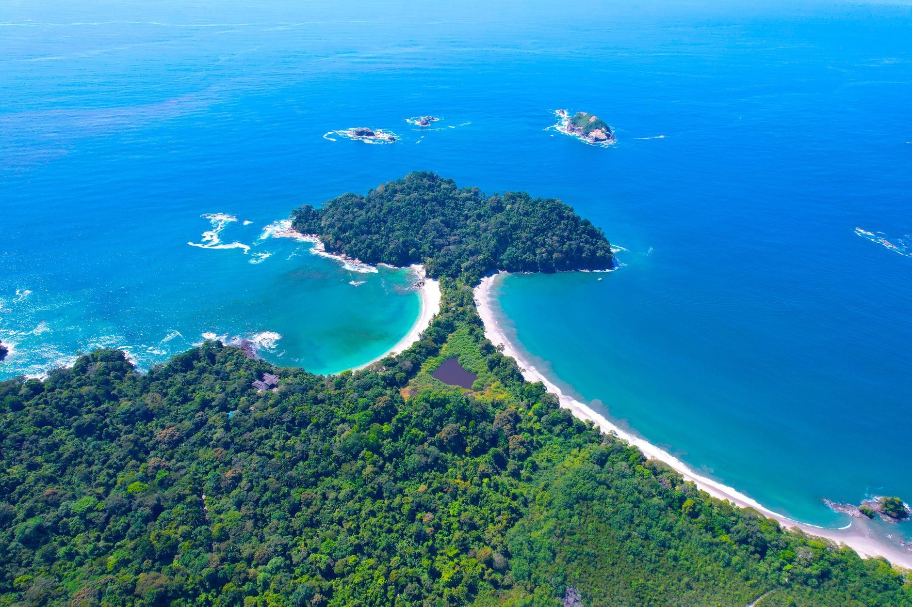 Luftaufnahme des bewaldeten Tombolos und der Strände des Nationalparks Manuel Antonio, umgeben von blauem Ozeanwasser.