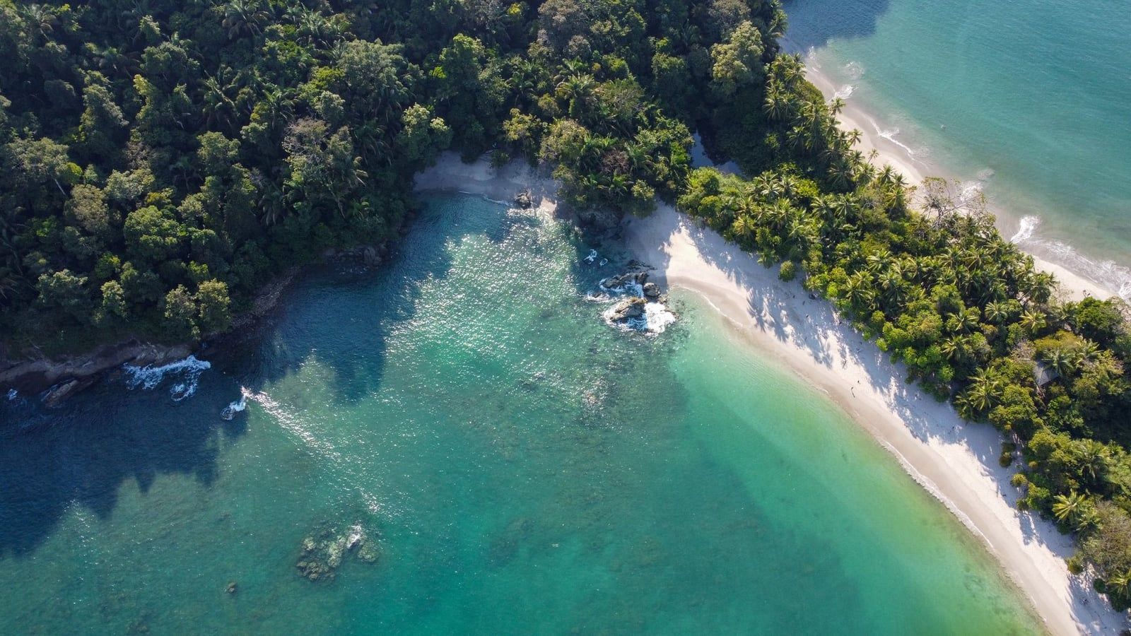Aerial view of the white sand and turquoise waters of Playa Manuel Antonio curving along the rainforest in Manuel Antonio National Park.