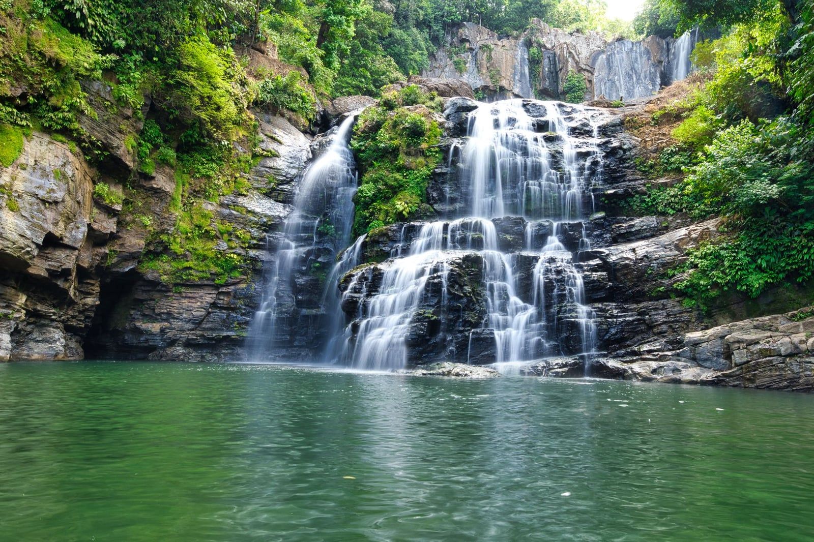 Die Nauyaca-Wasserfälle stufen sich über geschichtete Felsstufen in ein tiefgrünes Schwimmbecken nahe dem Manuel-Antonio-Nationalpark.