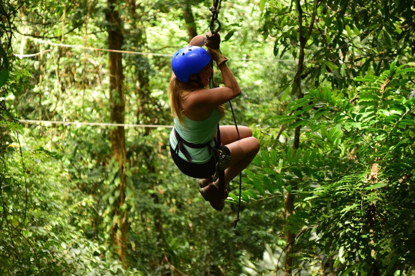 Eine Frau mit Helm fährt per Zipline durch das üppig grüne Regenwald-Blätterdach in Costa Rica.